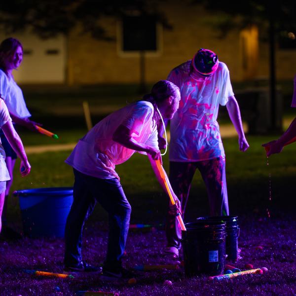 Blacklights shine on students who are wearing white T-shirts soaked in glowing neon paint.