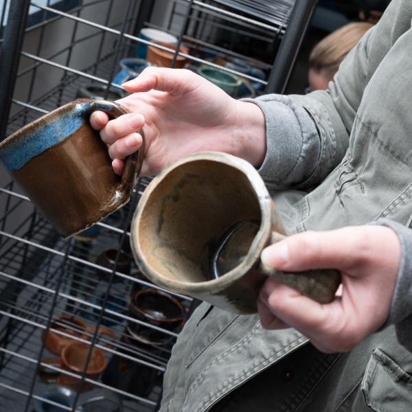 A close-up of a person's hands holding ceramic mugs.