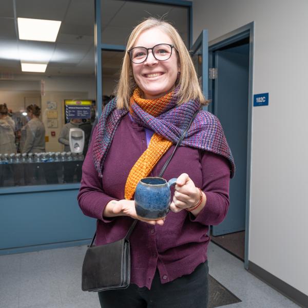 A woman holds a mug while smiling at the camera.
