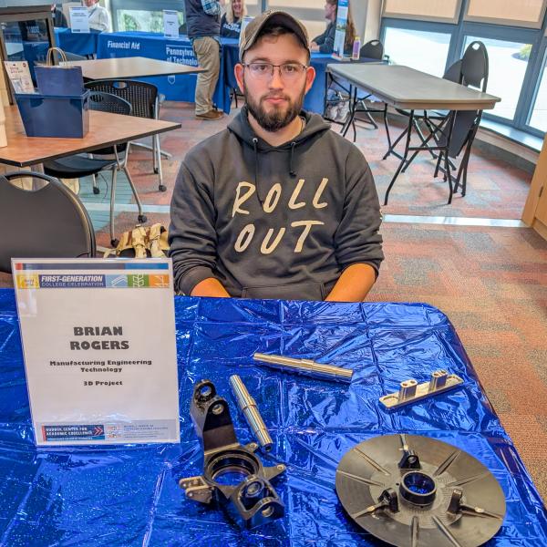 A student sits behind a table. On the table are metal vehicle components.