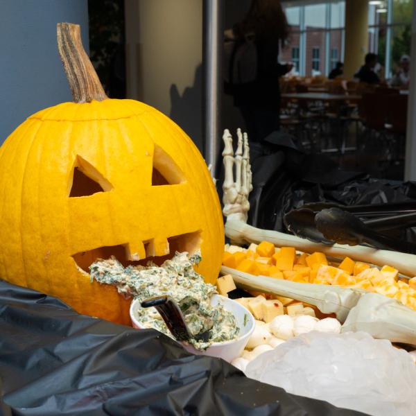 Spinach dip spills from the mouth of a jack-o'-lantern into a bowl.