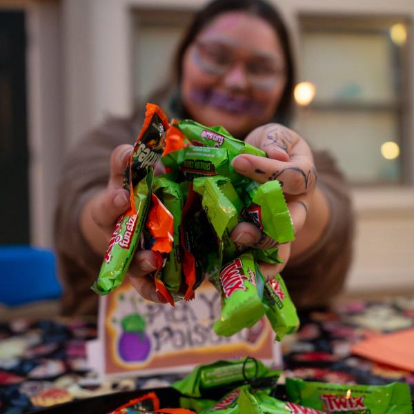 A student wearing face paint holds a handful of candy up to the camera.