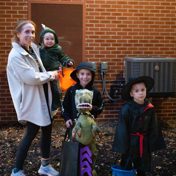 A mom with three children in costume. Two are dressed as dinosaurs, and one is dressed as Harry Potter.