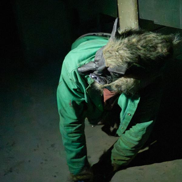 In a dark room, a student in a werewolf mask crawls on the floor.