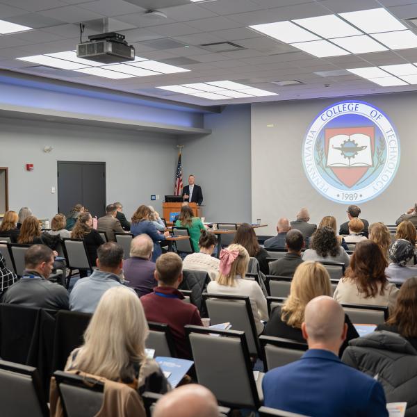 Penn College President Michael J. Reed speaks into a microphone before a full conference room.