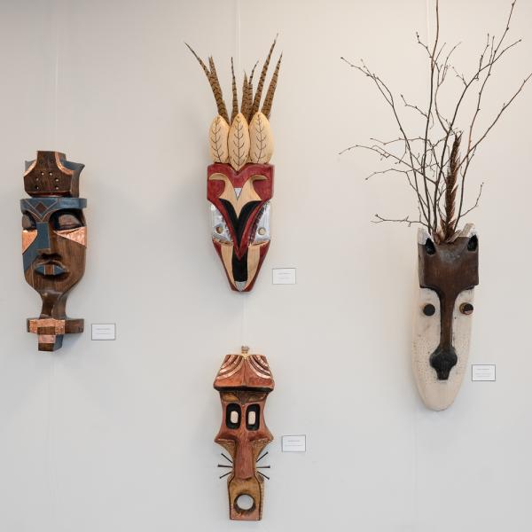 Four wooden masks hang on a white wall.