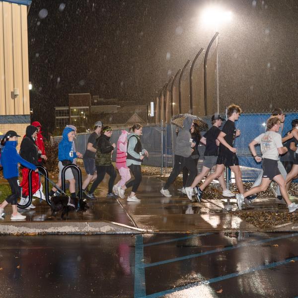 A large group of runners and walkers take off from a starting line near the Penn College Field House.
