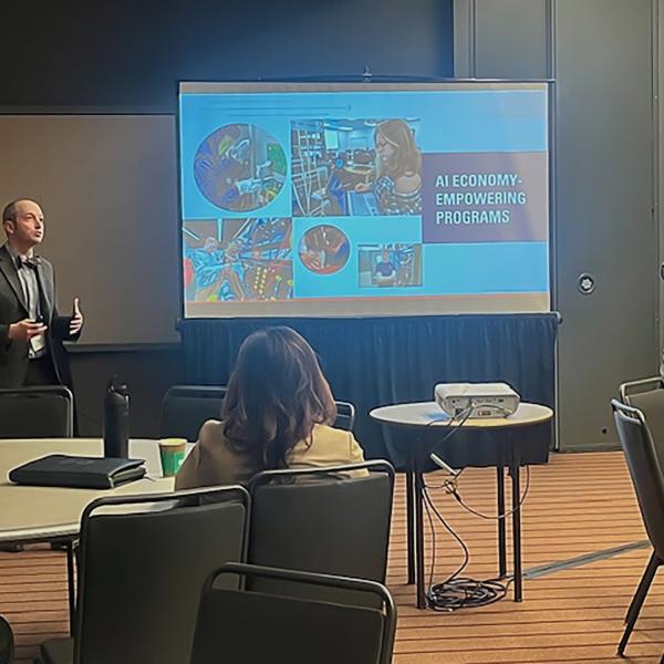 Two men stand on either side of a projector screen in a conference room.