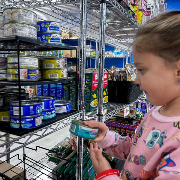 A child adds a can of tuna to a shelf.