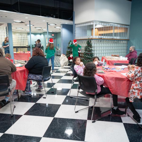 Families eat cookies and create crafts at round tables.