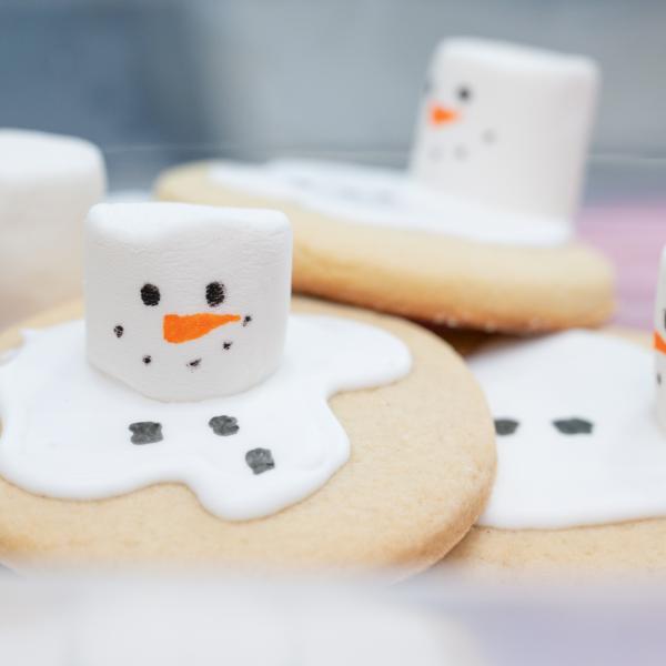 Close-up of sugar cookies decorated to look like melting snowmen, with white icing for melted snow and marshamallows for heads.