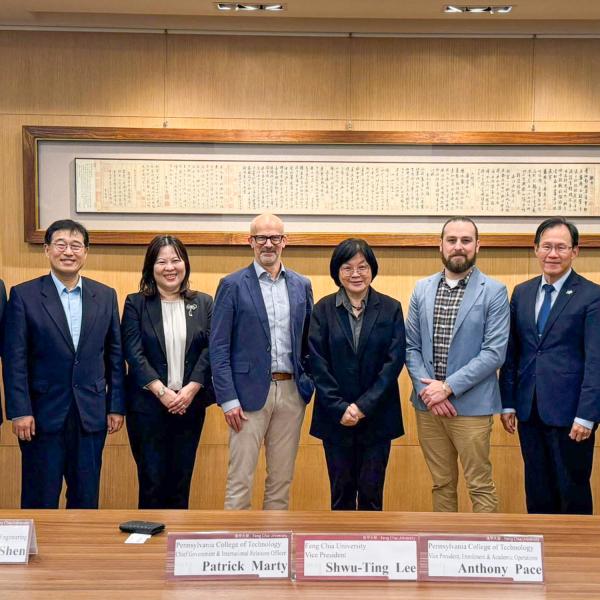 A group of men and women in business suits pose for a photo in a conference room.