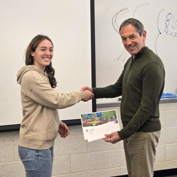 Two people shake hands. One is handing papers to the other.