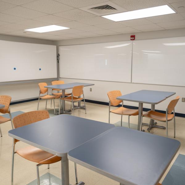A bright room with tables and chairs, and large whiteboards covering the walls.