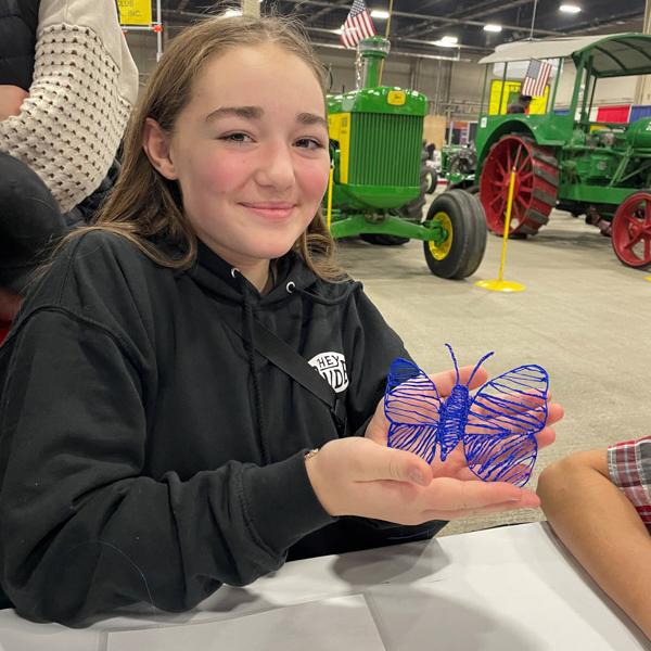 Child holds up a completed blue and purple 3D‑printed butterfly.