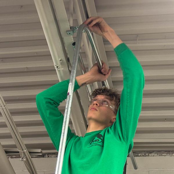 A student installs conduit on an open ceiling.