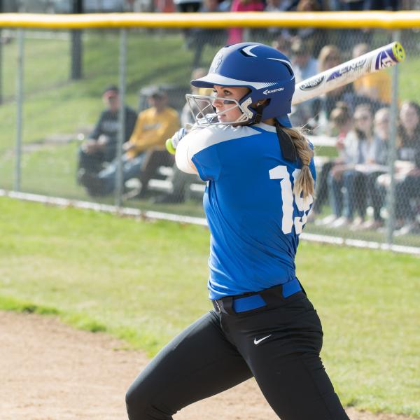 A softball player in a Penn College Uniform and batting helmet holds a bat over her shoulder in a batting stance.