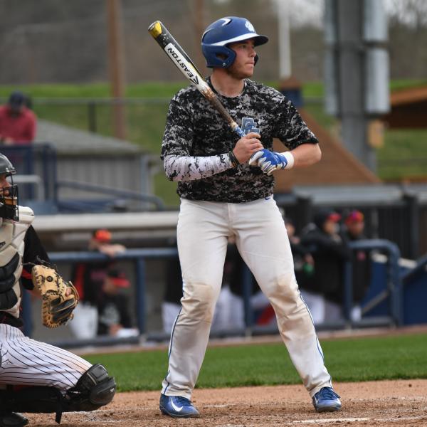 A baseball player in a Penn College uniform and batter helmet holds a bat in a batting stance.