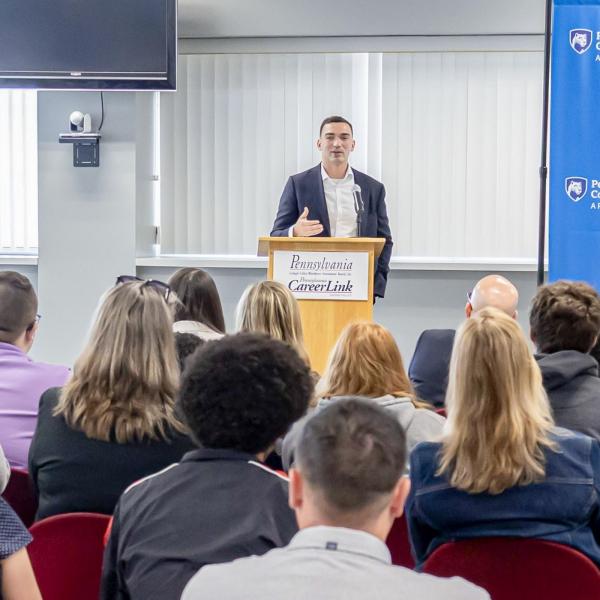 A man in a business suit stands at a lectern and speaks to an audience.