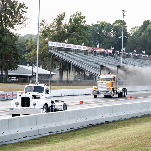 Two semi trucks travel down a drag-racing track at Maple Grove Raceway.