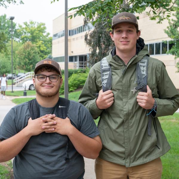 Two students carrying backpacks smile at the camera. Penn College's Breuder Advanced Technology & Health Sciences Center is visible behind them.