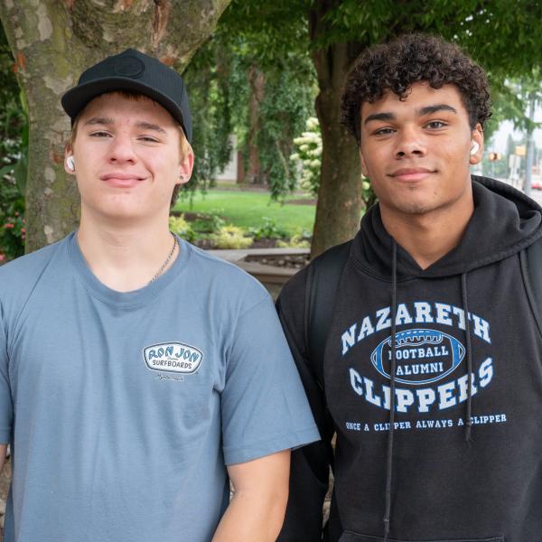 Two students smile. Trees on Penn College's Klump Academic Center patio are visible behind them.