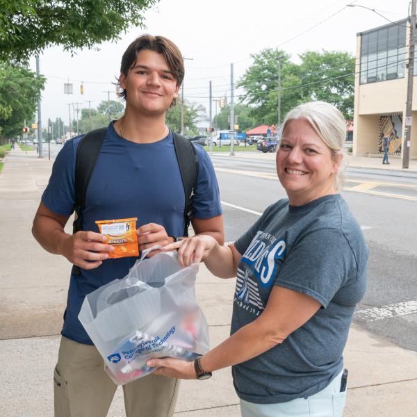 A student holds a snack-size bag of chips as an employee holds a large bag of snacks.