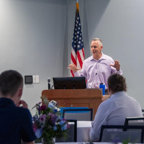 President Michael J. Reed speaks to a group of people seated at round tables in the college's Professional Development Center.
