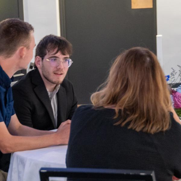 Three people sit at around table.