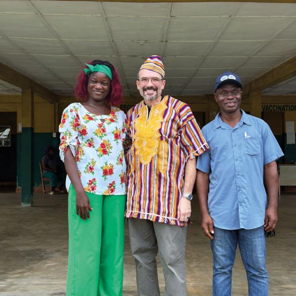 Three people pose for a photo at the entrance of a medical clinic in Liberia.