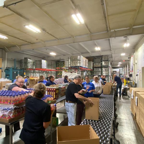 People add items to cardboard boxes as they slide down a conveyor.