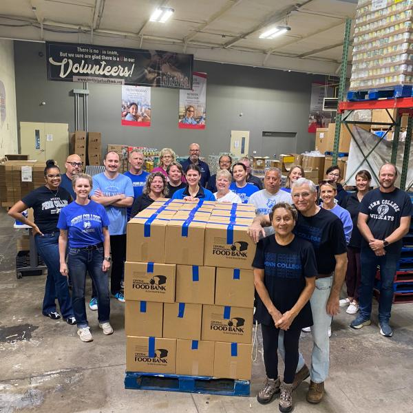 A group of people stand around a palate of cardboard boxes in a warehouse.