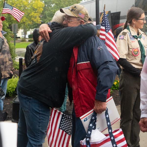 Two men hug outside the Penn College Bush Campus Center. One is holding a red white and blue tote bag with the Honor Flight Philadelphia logo.