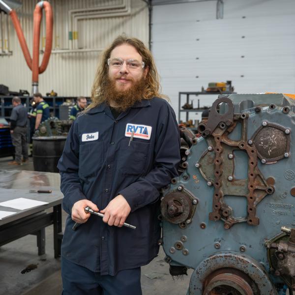 jake bus mechanic apprentice leaning on motor smiling
