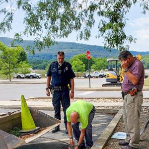 General Services' Brooke M. Barton prepares to lift the grate for Miller (at right), joined on the scene by Penn College Police Officer Jeffrey E. Kriner.