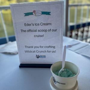 A partly eaten dish of mint green-colored ice cream on a table. A small sign behind the dish reads: Eder's Ice Cream: The official scoop of our cruise! Thank you for crafting Wildcat Crunch for us!