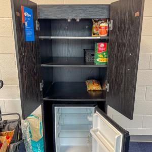 The mini cupboard, a cabinet that contains shelving and a mini refrigerator, in the Hager LIfelong Education Center with open doors and near-empty shelves.