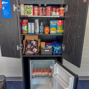 The mini cupboard, a cabinet that contains shelving and a mini refrigerator, in the Hager LIfelong Education Center with open doors and full shelves.