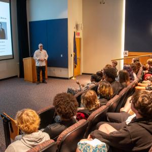 A man in chefs whites speaks in at the front of an auditorium.