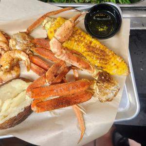 A rectangular plate filled with crab legs in the center. One corner has corn on the cob, another has shrimp, and another has a baked potato.