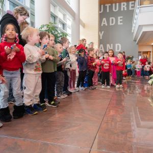 Preschool-aged children wearing red and green sing songs and ring jingle bells.