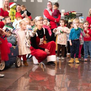 Preschool-aged children wearing red and green sing songs and ring jingle bells.