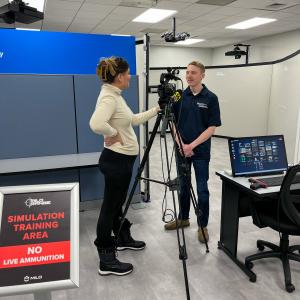 A student talks with a reporter who is holding a microphone and operating a TV camera.
