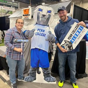 Two people stand with a cut-out of the Penn College Wildcat mascot.