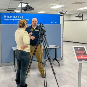An instructor talks with a reporter who is holding a microphone and operating a TV camera.