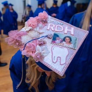 A graduation cap is decorated with a glittery pink background, pink flowers, a large white tooth, a photo of children holding toothbrushes and the letters "RDH," which stands for registered dental hygienist.