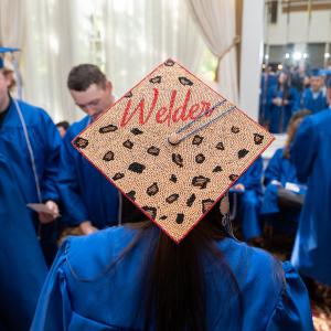 A woman wears a graduation cap that is decorated with gold beads, leopard spots and the world "Welder."