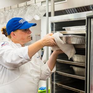 A woman in a chef uniform pulls a tray of food from a rack.