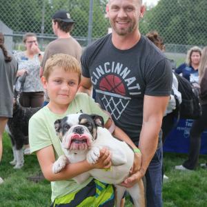 A man helps a child to hold up a small dog. The dog is sticking out its tongue.
