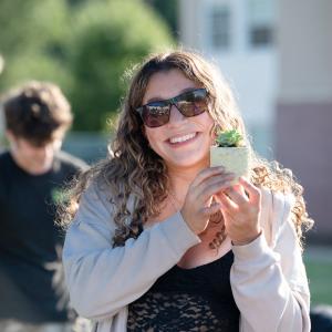A student smiles and holds up a plant in a small decorative pot.